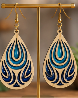 A pair of teardrop-shaped wooden dangle earrings with intricate blue and black cutout patterns, hanging from a gold-colored metal stand.