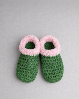 Green crochet slippers with pink fuzzy tops on a gray background