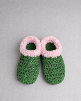Green crochet slippers with pink fuzzy tops on a gray background