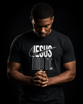 A man wearing a black t-shirt with a white graphic that reads 'JESUS DID IT.' against a solid black background.