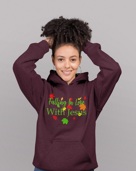 A woman smiling and posing with a maroon t-shirt or hoodie featuring the text 'FALLING IN LOVE WITH JESUS' and green and red leaf graphics on the front.