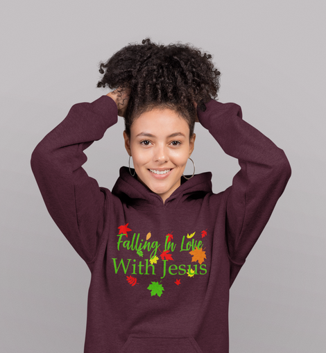 A woman smiling and posing with a maroon t-shirt or hoodie featuring the text 'FALLING IN LOVE WITH JESUS' and green and red leaf graphics on the front.